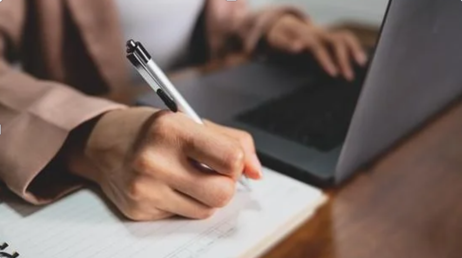 A content writer drafting copy by hand beside a laptop